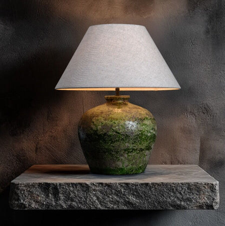 Table lamp with a textured green base and white shade on a stone surface against a dark background