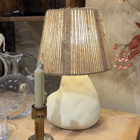 Pebble shaped stoneware lamp with a string jute shade on a wooden cabinet