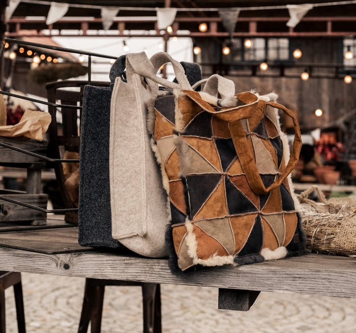 Four pure wool tote bags in grey, charcoal, stone and beige against a white wood panelled background