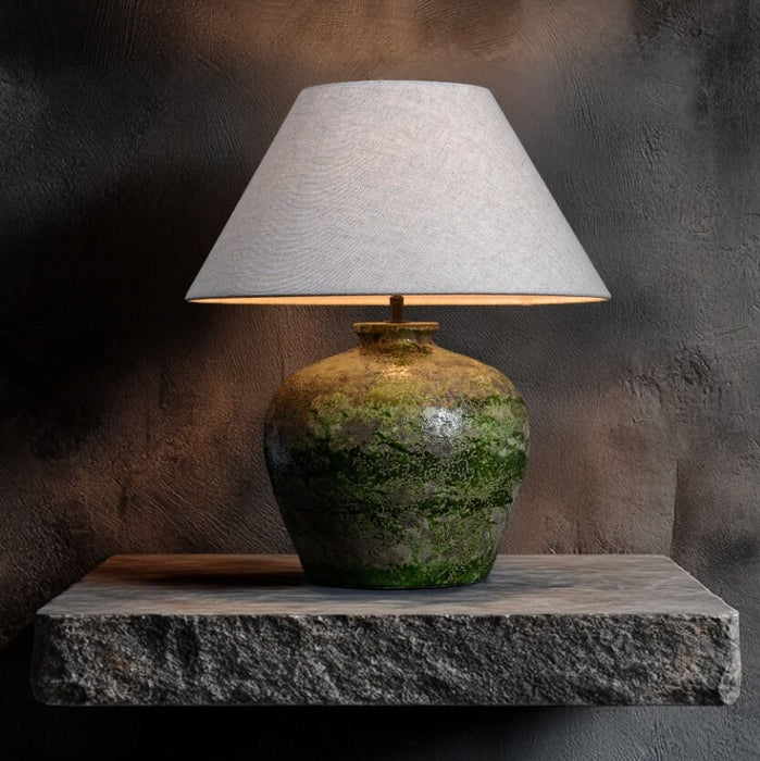 Table lamp with a textured green base and white shade on a stone surface against a dark background