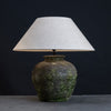 Handcrafted table lamp with textured green base and natural linen lampshade on a dark background