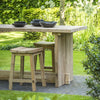 A wooden bar table with a small stool beside it, placed on a garden pathway, with a bowl and glassware on the table.
