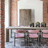 A large rectangular dining table made from reclaimed wood with an aged patina, positioned in a room with exposed brick walls and a wooden door.