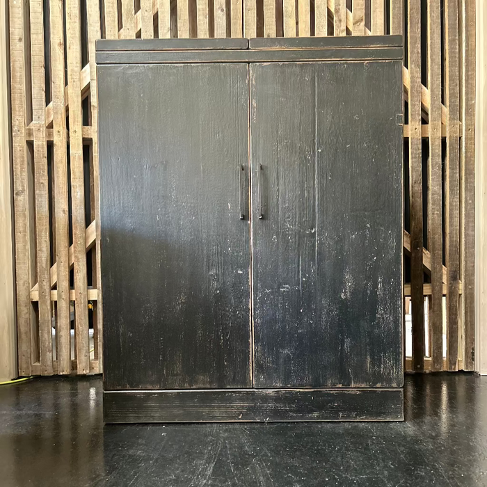 A black wine cabinet with two doors and opening tops, made of old pine wood, positioned against a wooden backdrop.
