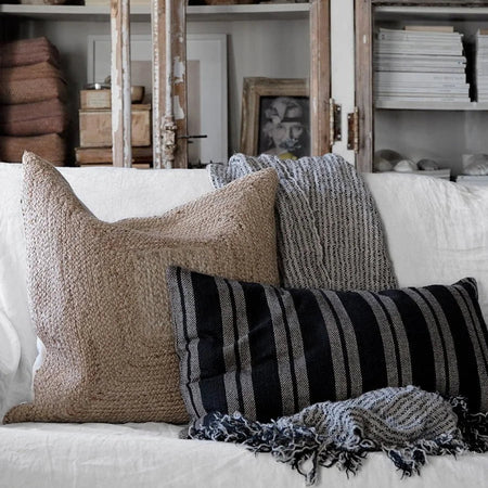 Decorative pillows and a striped linen throw on a sofa with a bookshelf in the background