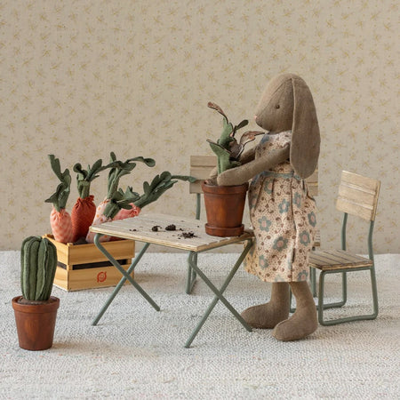 Stuffed rabbit in a floral dress tending to plants in a miniature room setting.