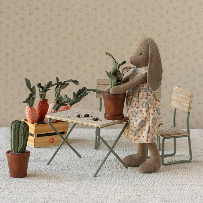 Stuffed rabbit in a floral dress tending to plants in a miniature room setting.