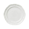 A white matte dinner plate with a wavy edge on a plain background.