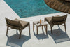 Two teak and wicker easy chairs by Gommaire with a small table beside a pool and straw sun parasol