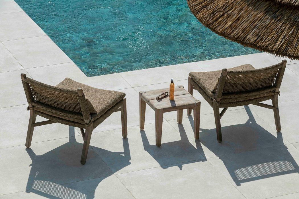 Two teak and wicker easy chairs by Gommaire with a small table beside a pool and straw sun parasol
