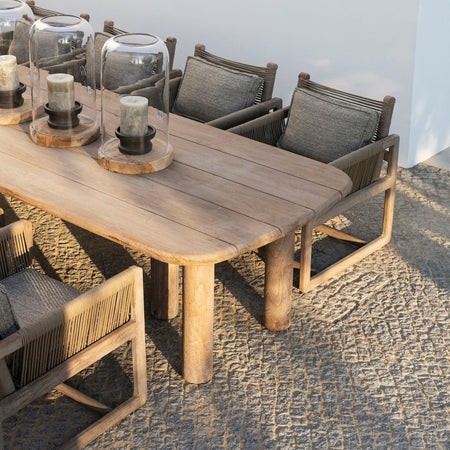 Low teak outdoor dining table with chairs and candle holders on a textured surface.