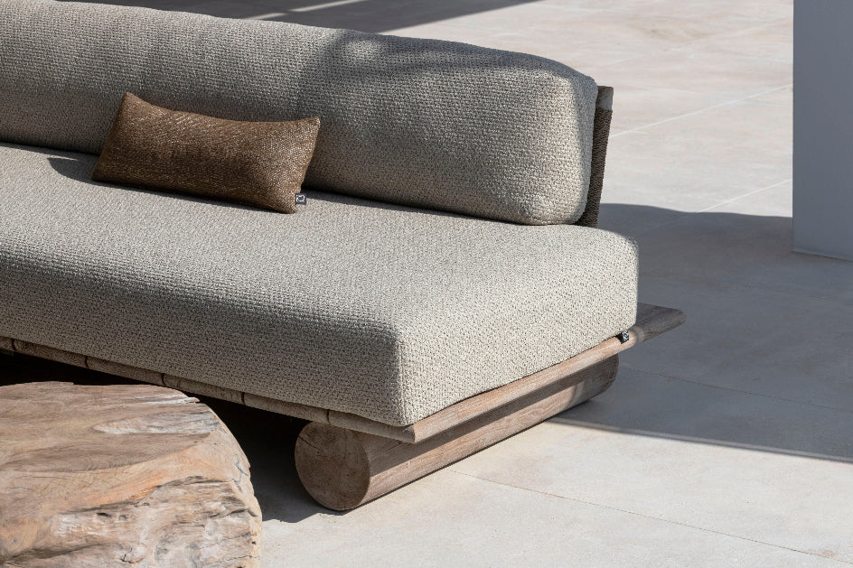 Solid teak outdoor sofa with beige cushions on pale floor with teak rootball table in foreground