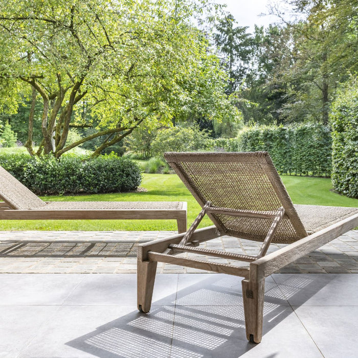 Teak and woven rattan sunlounger on a patio with greenery in the background
