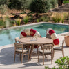 Outdoor setting with a wooden table and chairs by a pool, surrounded by greenery.