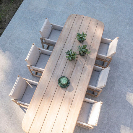 Outdoor teak dining table and teak armchairs on a concrete patio.