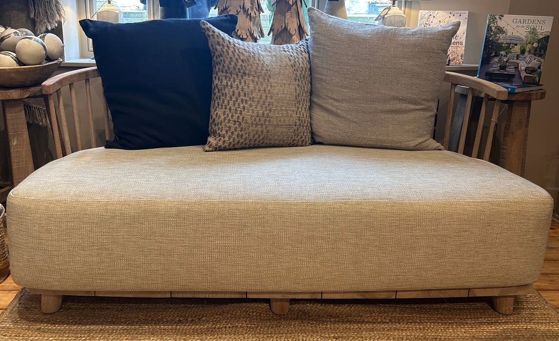 A contemporary 2-seater lounge sofa with a natural grey patina teak frame and outdoor fabric cushions, displayed in a shop setting.