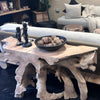 A natural grey teak root console table with items on top, placed against a room setting with a sofa and cushions.