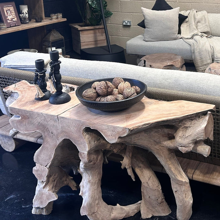 A natural grey teak root console table with items on top, placed against a room setting with a sofa and cushions.