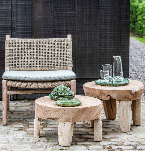 Chunky solid teak side tables next to outdoor wicker and teak lounge chair with decorative plates and glassware