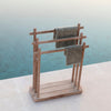 A teak towel rack by Gommaire with a shelf and a lower bench, placed near a swimming pool with towels hanging on it.