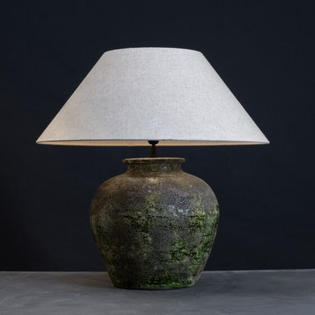 Handcrafted table lamp with textured green base and natural linen lampshade on a dark background