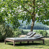 Outdoor teak daybed with cushions under a tree in a garden setting