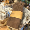 Dark brown suede women's gloves by Shepherd of Sweden lined with pure sheepskin on a table surrounded by more gloves in Shepherd branded tissue paper