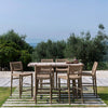 Outdoor teak bar table set with table and six bar seats  on a patio with a scenic backgr