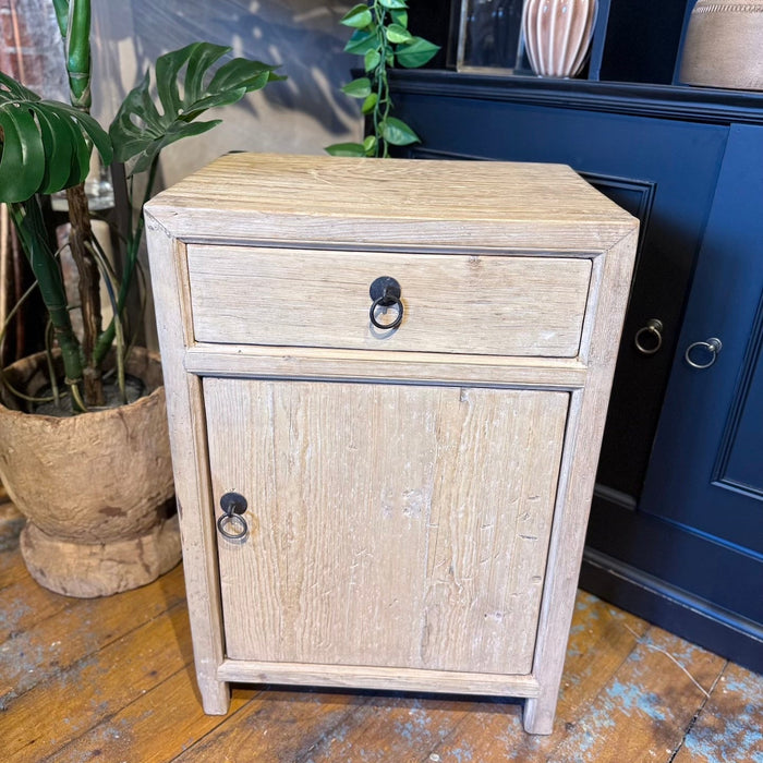 Small wooden cabinet on wood floor with plant in background