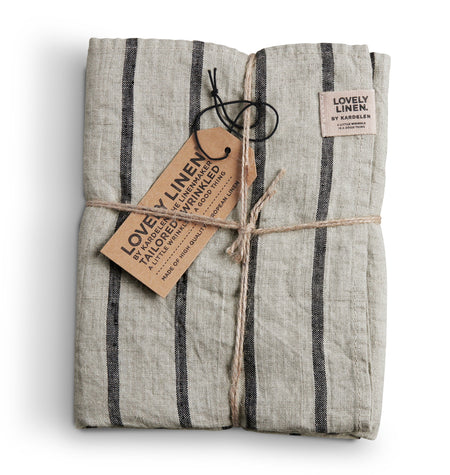 A linen table runner with black stripes, tied with a string and a tag showing the brand name 'Lovely Linen'.