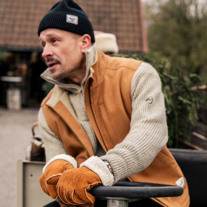 Man wearing a brown vest and gloves sitting outdoors