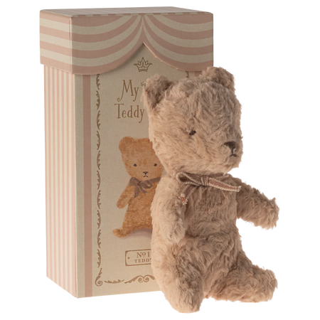 Teddy bear with a bow tie in front of a striped box labelled 'My First Teddy'.