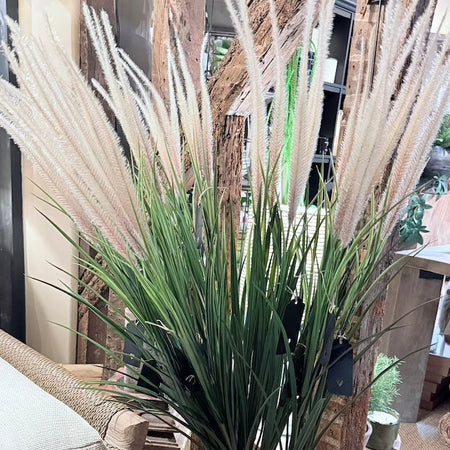 Ornamental grasses in a decorative vase on a wooden floor with a textured wall in the background