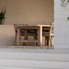 Outdoor seating area with wooden table and chairs against a white wall.