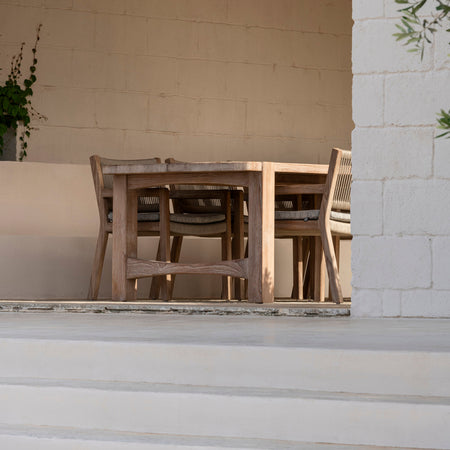 Outdoor seating area with wooden table and chairs against a white wall.