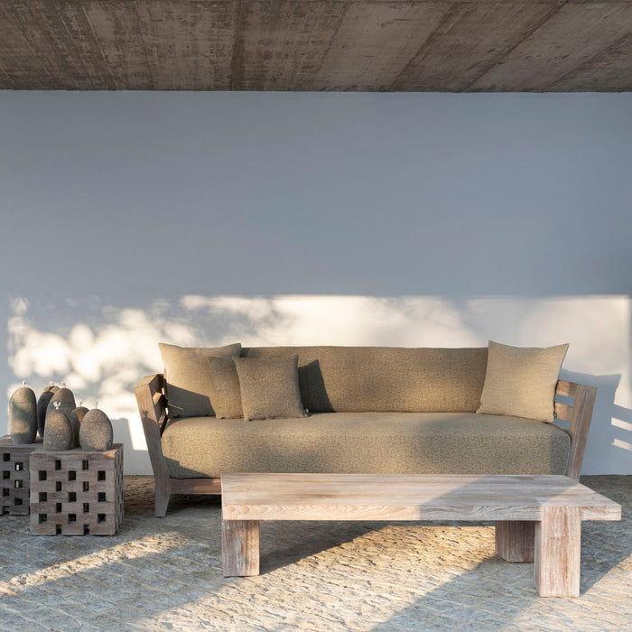 Modern outdoor furniture set with a sofa and teak coffee table on a concrete floor.