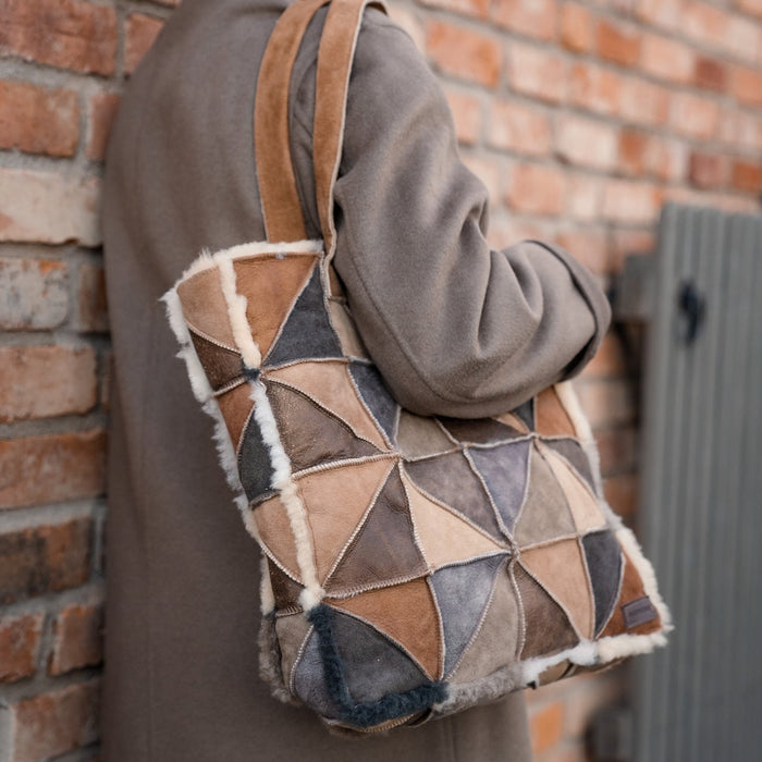 Person carrying a sheepskin patchwork shopping bag against a brick wall.