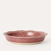 A round, pink glazed pie dish with a floral pattern on the bottom surface, made from durable white stoneware clay.