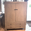 A tall reclaimed elm armoire cabinet with two upper doors and four lower drawers, featuring a dark metal pull handle and round drawer knobs, set in a home interior.