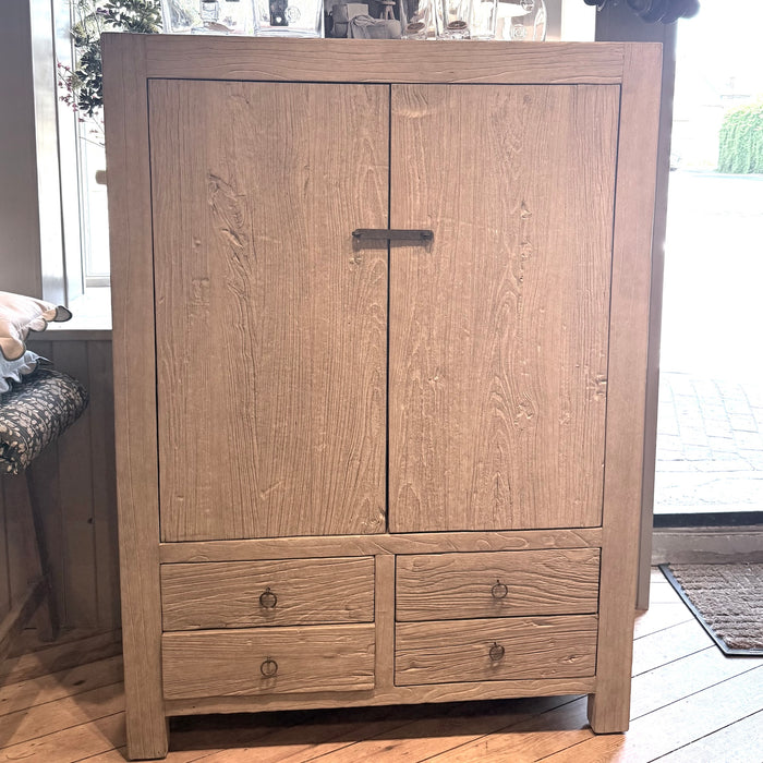 A tall reclaimed elm armoire cabinet with two upper doors and four lower drawers, featuring a dark metal pull handle and round drawer knobs, set in a home interior.