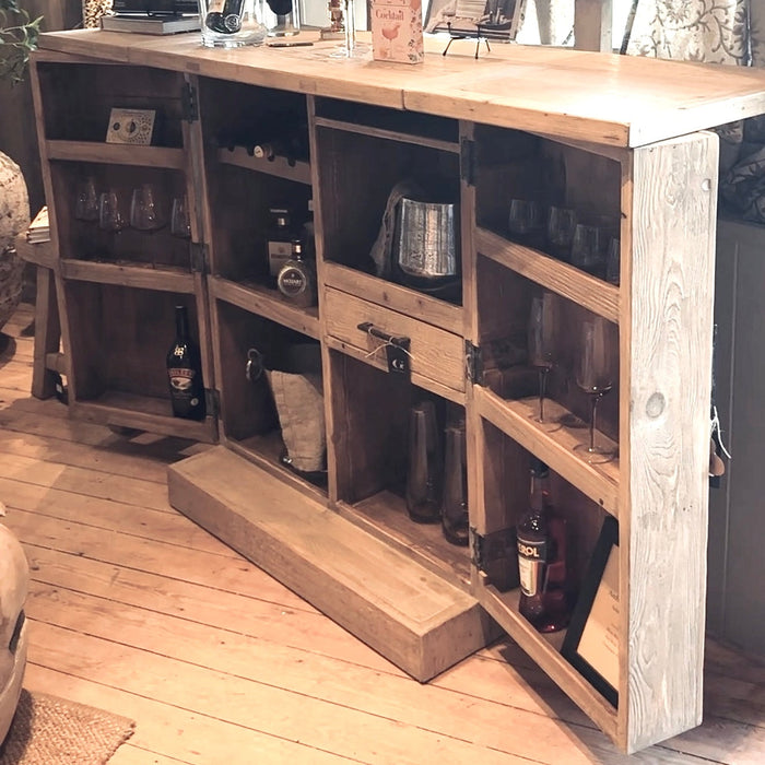 Wooden bar cart with shelves and bottles in a home setting