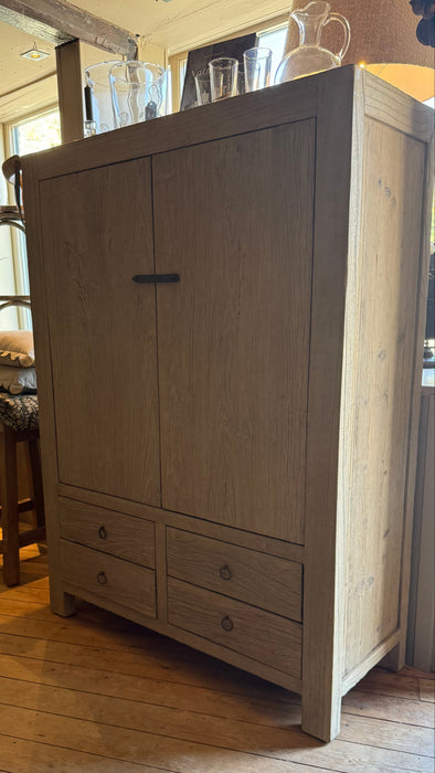 A tall light reclaimed elm wood armoire cabinet with two upper doors and four lower drawers, shown in a rustic room with wooden floors.