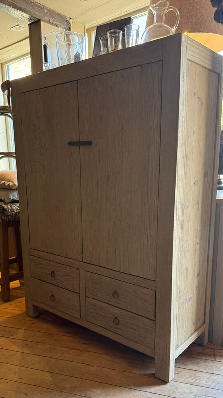 A tall light reclaimed elm wood armoire cabinet with two upper doors and four lower drawers, shown in a rustic room with wooden floors.