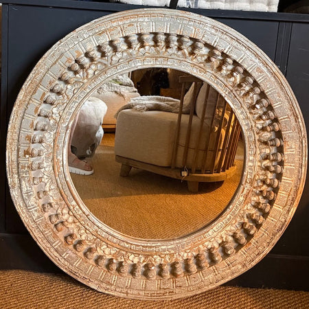 Grey distressed mirror with ornate detailing against a black cupboard on jute flooring