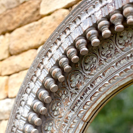 Detail of ornate carving on round mirror against outdoor brick wall