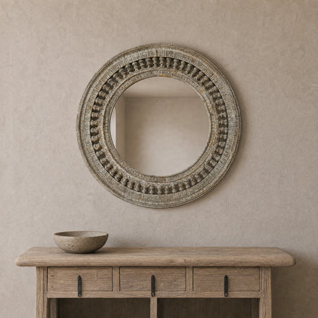 Distressed ornately carved mirror on beige wall above rustic wooden console with bowl