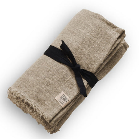 Beige linen tablecloth tied with black ribbon and frayed edge design with Lovely Linen brand label on white background