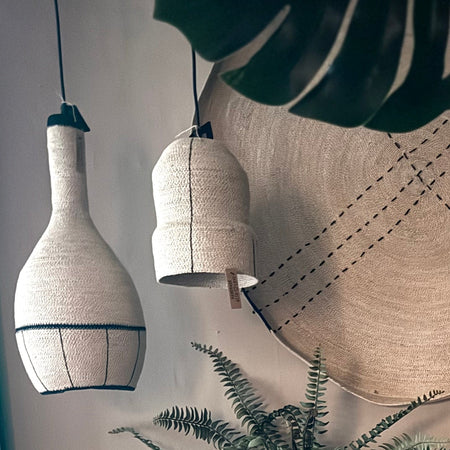 Textured pendant lights hanging against a neutral wall with plants