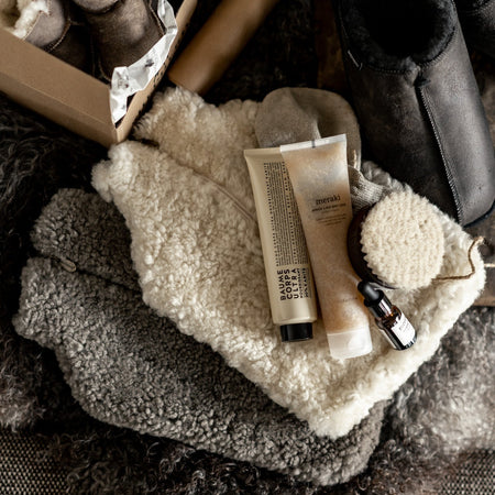Cream and grey sheepskin hot water bottles with body brush and lotions on a fluffy throw