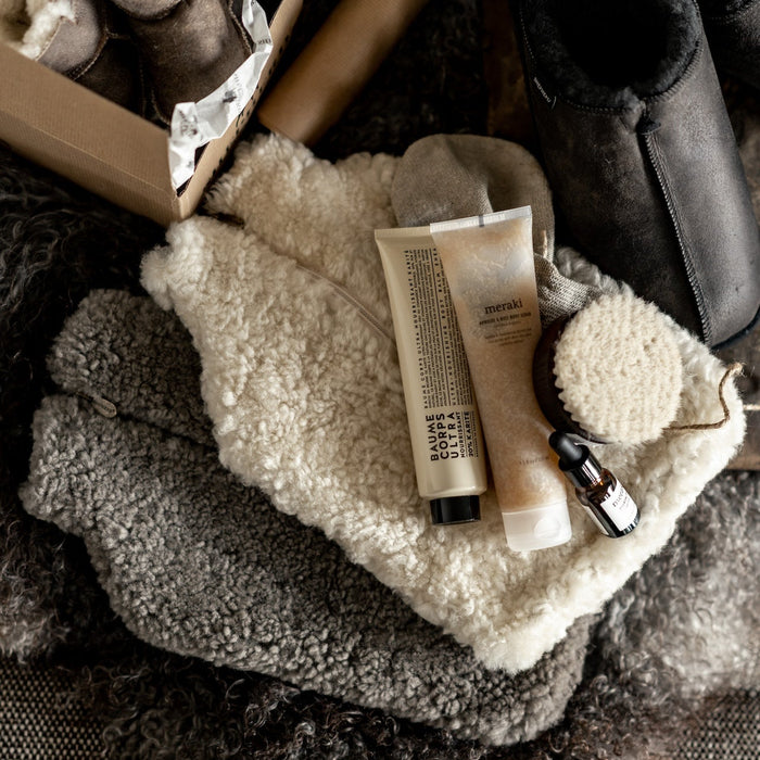 Cream and grey sheepskin hot water bottles with body brush and lotions on a fluffy throw
